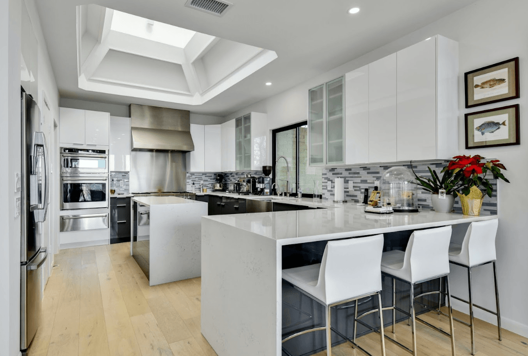 A kitchen with white cabinets , stainless steel appliances , a large island , and a skylight.