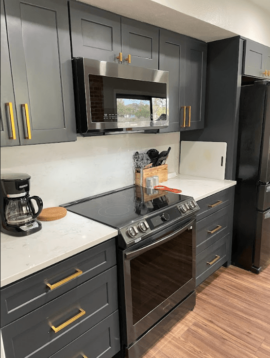 A kitchen with gray cabinets , black appliances , a stove , microwave , and refrigerator.