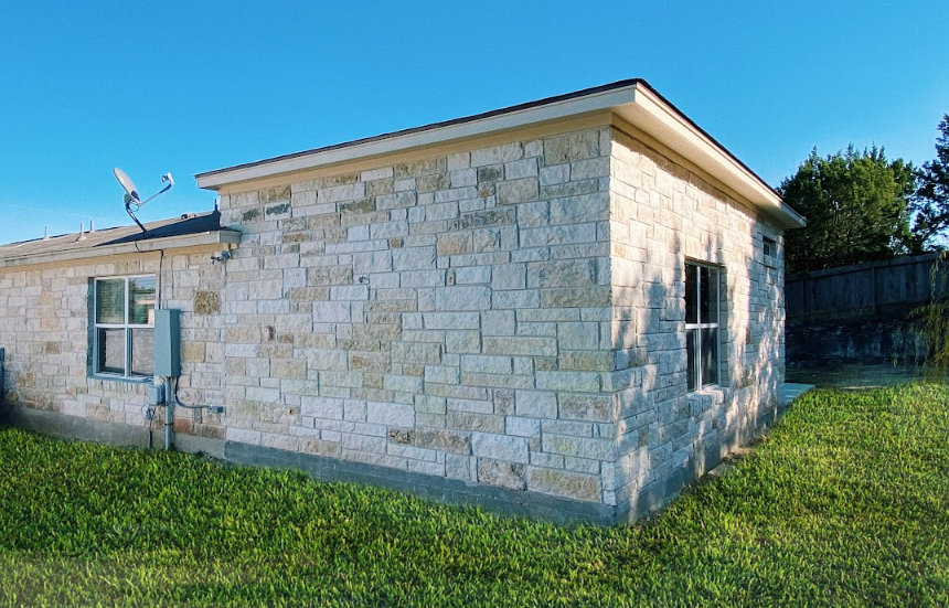 A small stone house with a satellite dish on the roof is sitting in the middle of a lush green field.