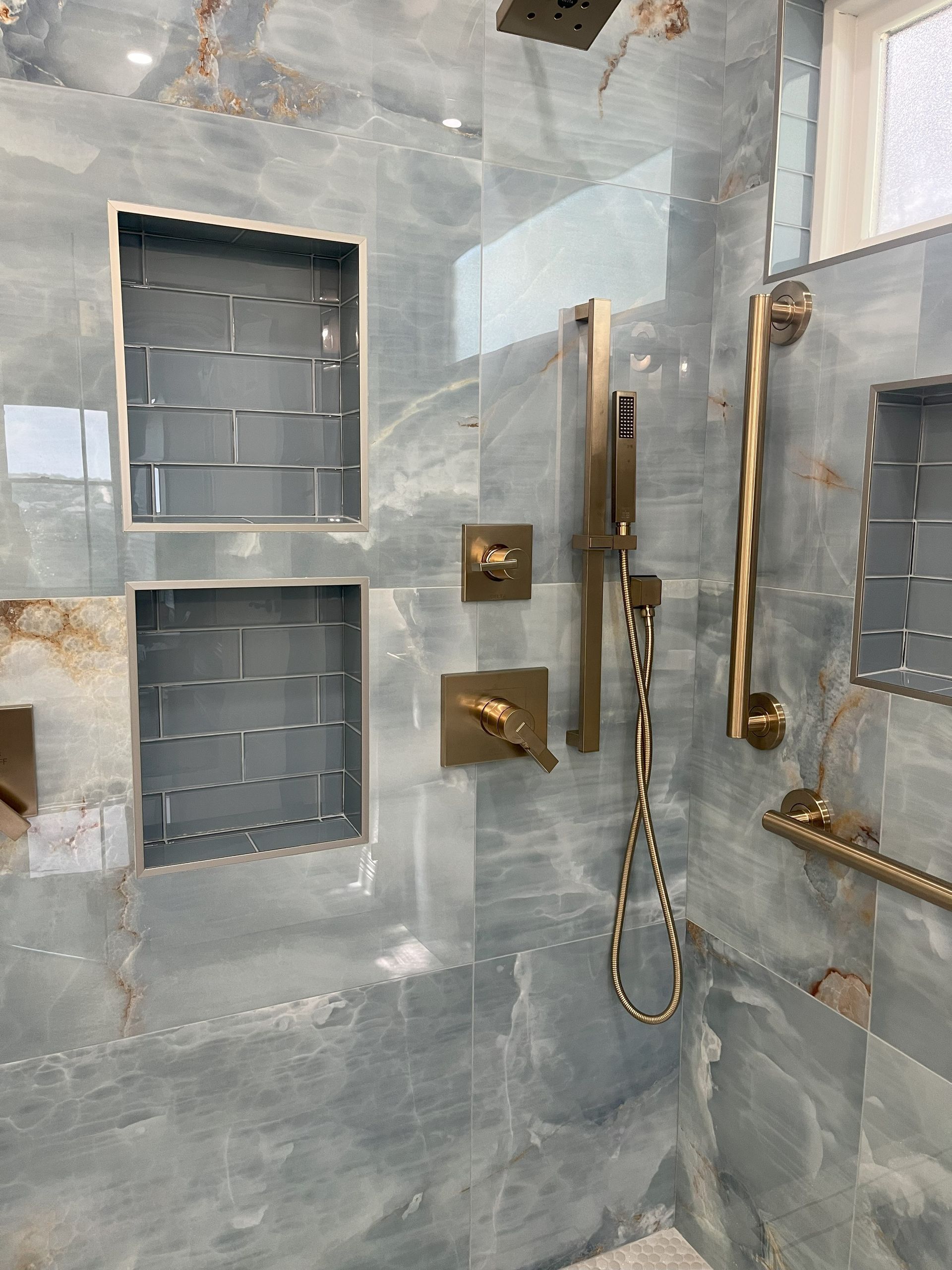 A bathroom with a walk in shower and a brass shower head.