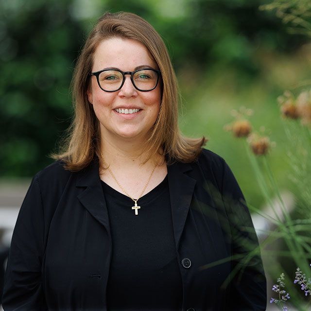 Eine Frau mit Brille und einer Kreuzkette lächelt in die Kamera.