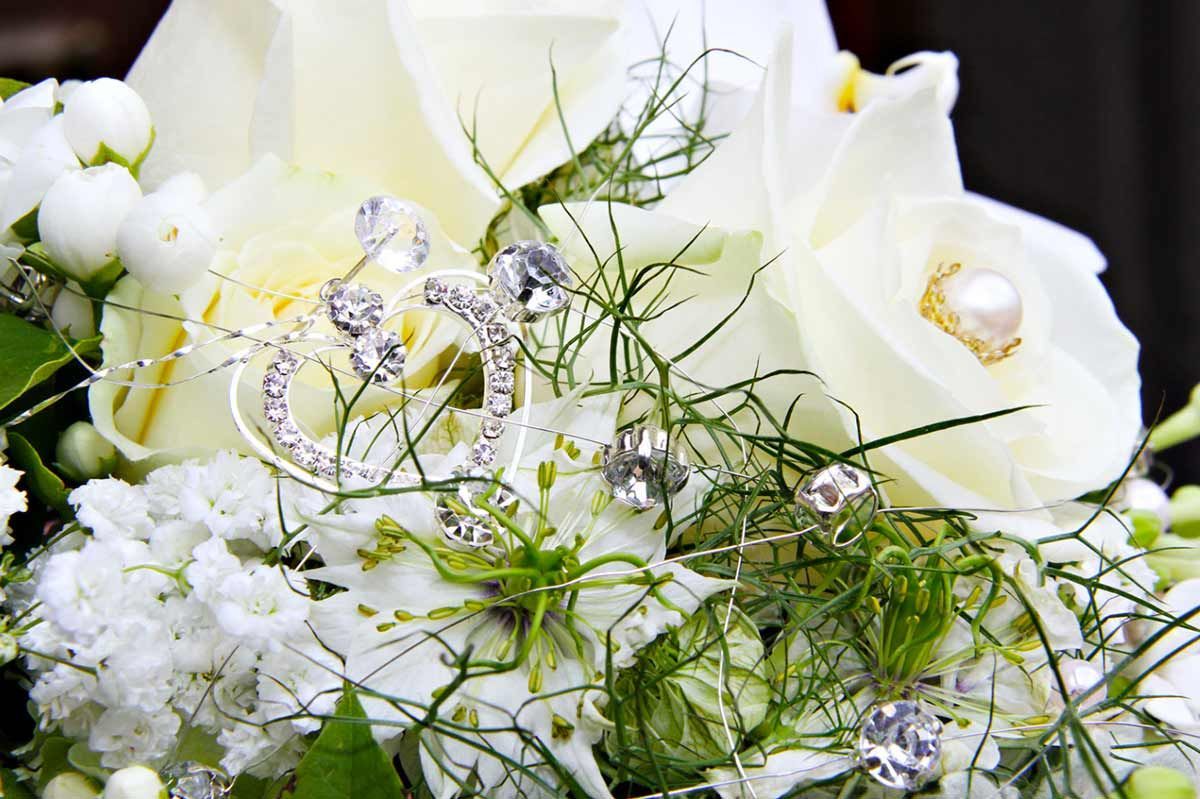 Eine Nahaufnahme von einem Strauß weißer Rosen mit Eheringen und einer Tiara