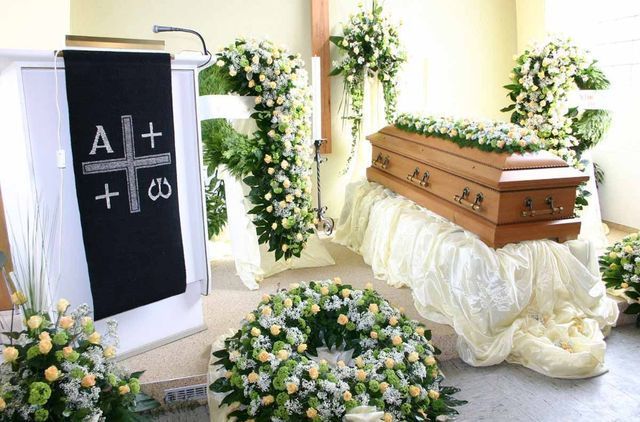 Ein Sarg steht auf einem Tisch in einer Kirche, umgeben von Blumen - eine Erdbestattung.