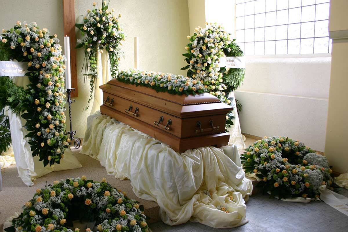 Ein Sarg steht auf einem Tisch in einem mit Blumen geschmückten Raum.