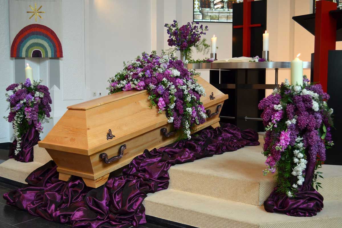 In einer Kirche ist ein Sarg mit violetten und weißen Blumen geschmückt.