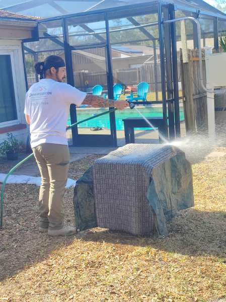 A man is spraying water on a rock in a backyard.