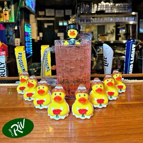 A group of rubber ducks are sitting on a bar next to a glass of beer.