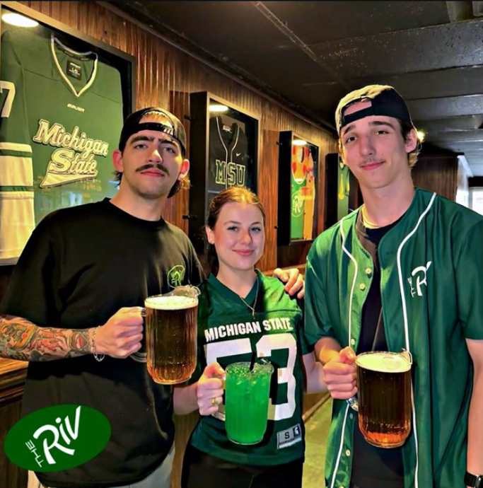 A man in a michigan state jersey is holding a beer mug