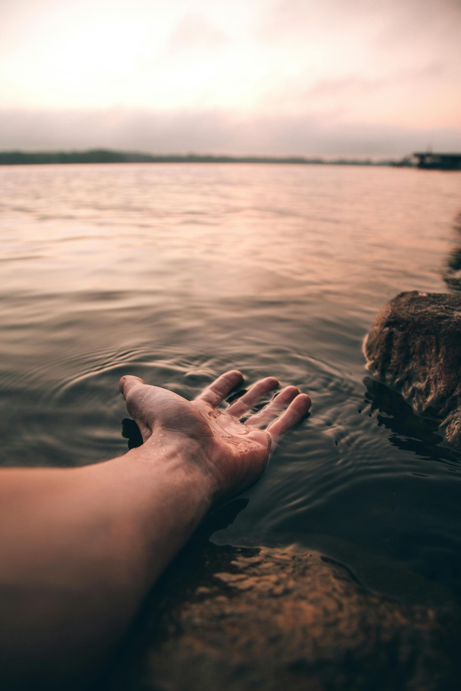 A person is reaching out their hand into the water.