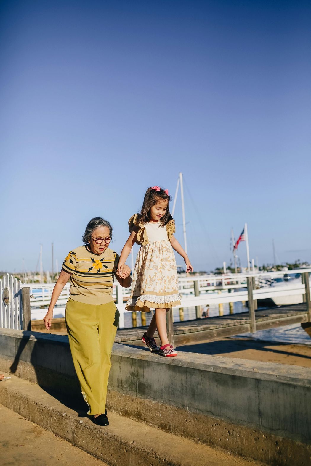 An elderly woman and a little girl are walking down stairs holding hands.