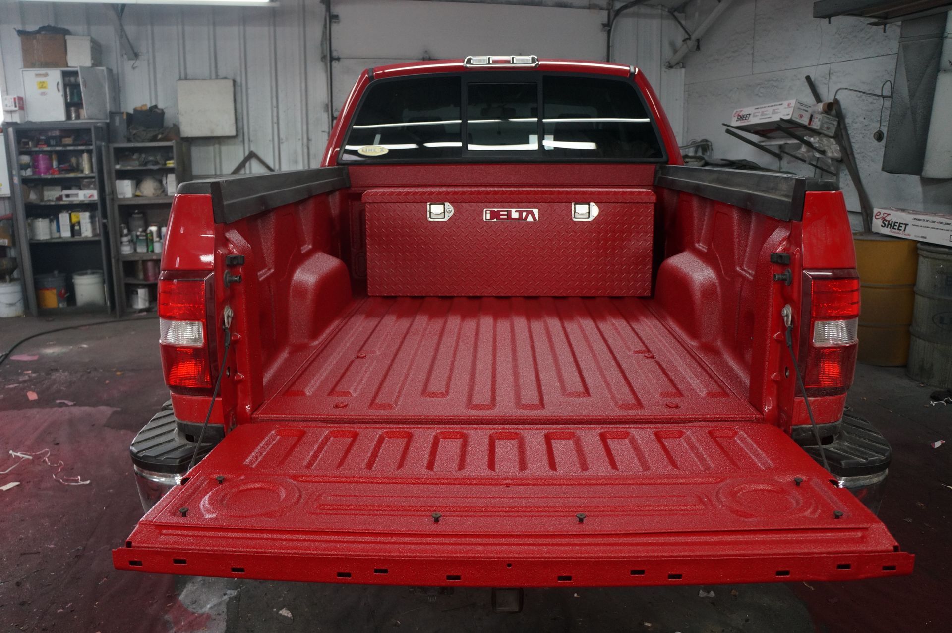 Benne de pick-up rouge avec hayon ouvert, coffre à outils et revêtement texturé.