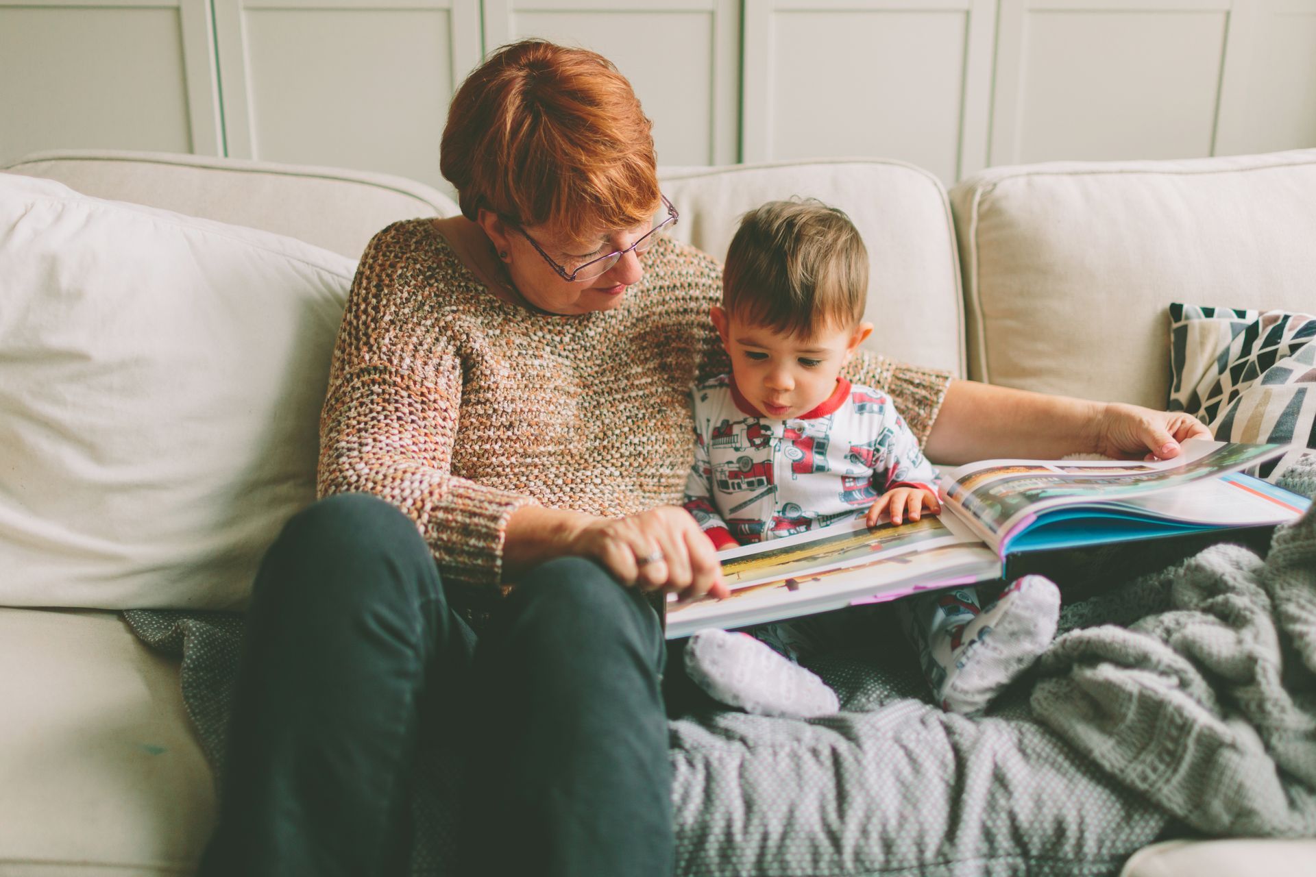 A woman is sitting on a couch reading a book to a baby.