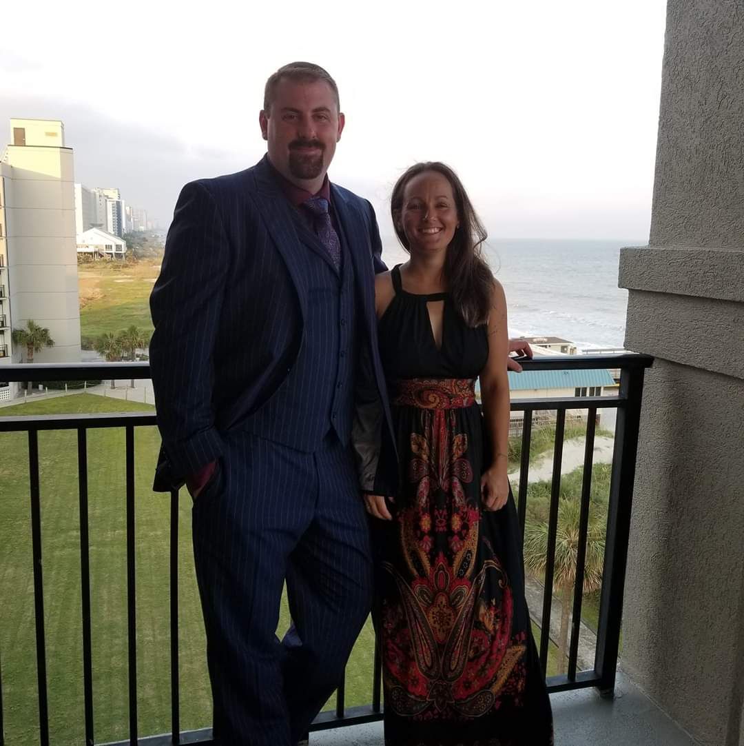 A man and a woman standing on a balcony overlooking the ocean