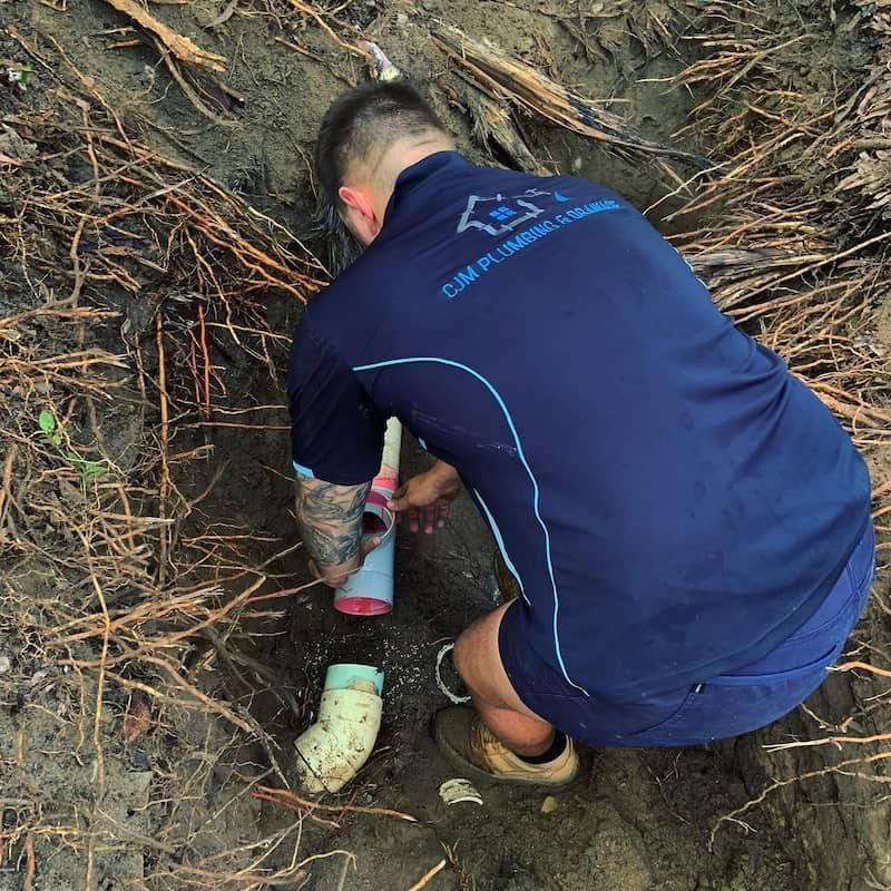 A Pipe is Laying in the Dirt in a Hole — CJM Plumbing & Roofing Mackay in Mackay, QLD