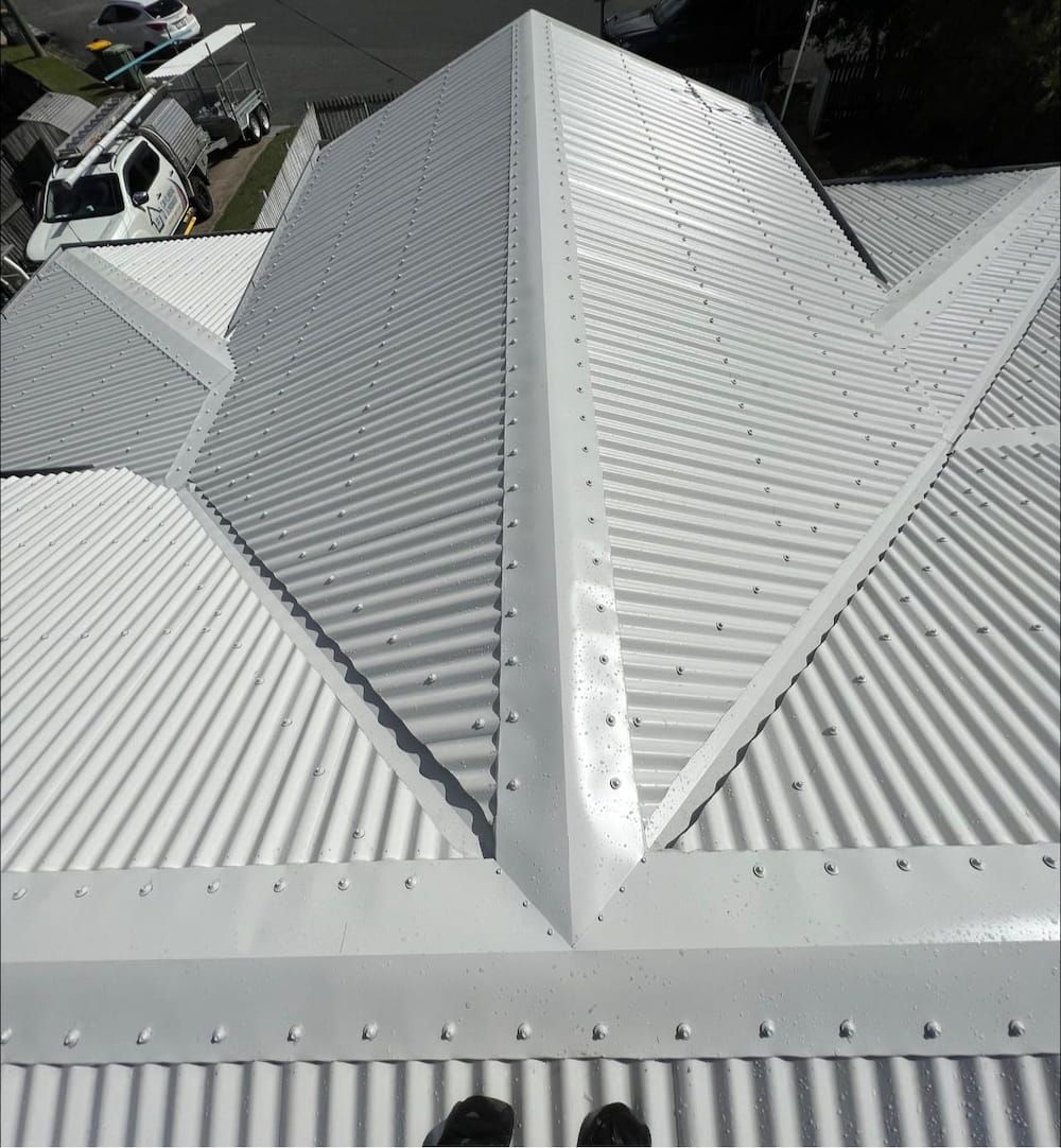 A Person is Standing on the Roof of a White House — CJM Plumbing & Roofing Mackay in Mackay, QLD