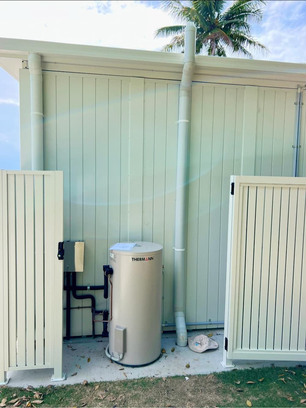 A Water Heater is Sitting in Front of a White Fence — CJM Plumbing & Roofing Mackay in Mackay, QLD