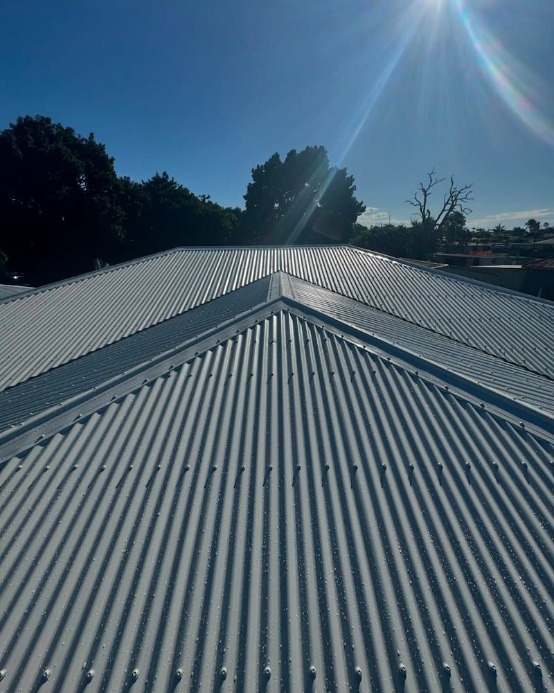 A White Corrugated Metal Roof With Trees in the Background on a Sunny Day — CJM Plumbing & Roofing Mackay in Mackay, QLD