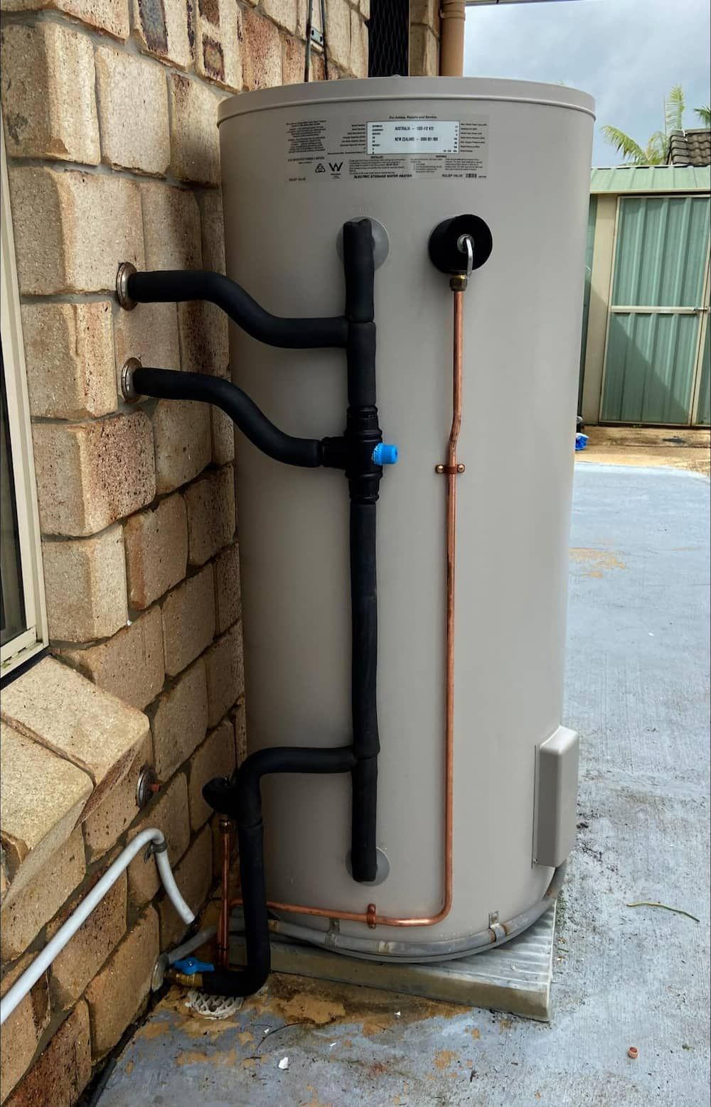 A Water Heater is Sitting on the Side of a Brick Building — CJM Plumbing & Roofing Mackay in Mackay, QLD