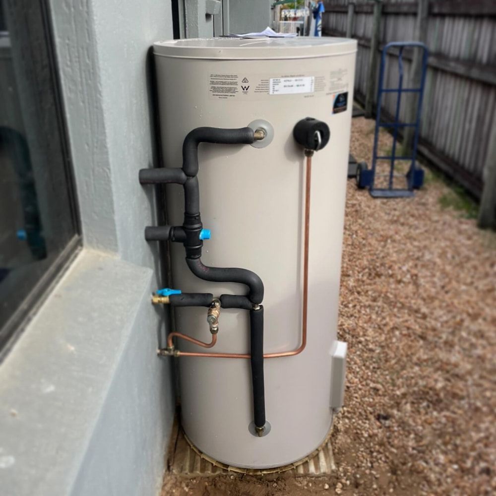 A Water Heater is Sitting on the Side of a Building Next to a Window — CJM Plumbing & Roofing Mackay in Mackay, QLD