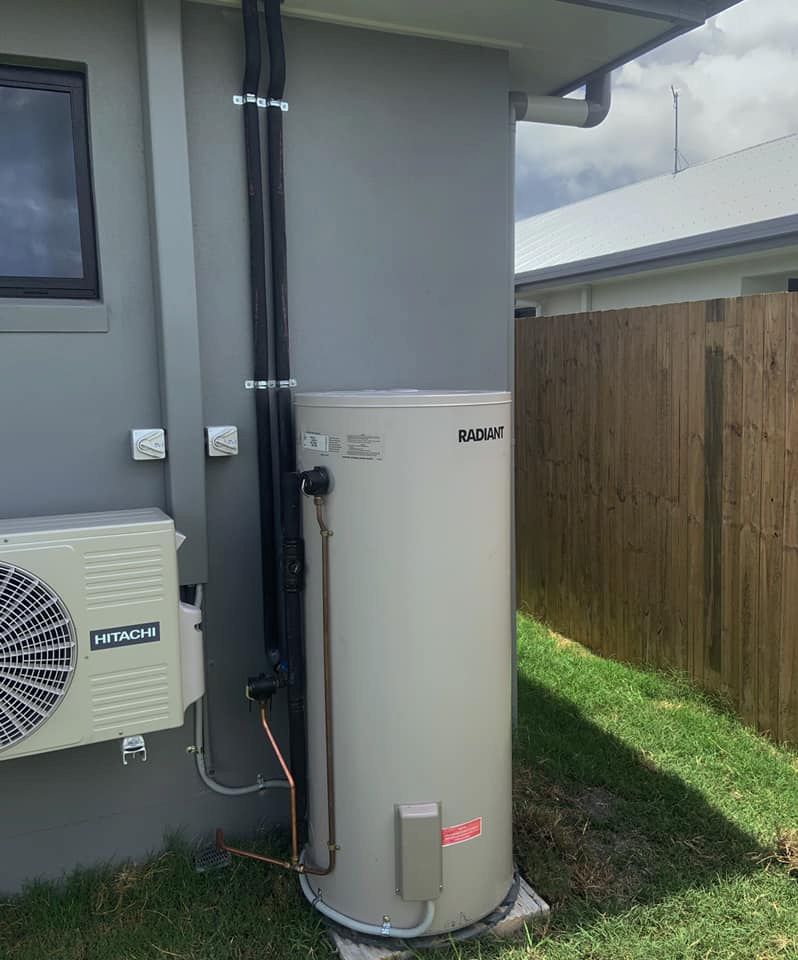 A White Water Heater is Sitting on the Side of a House Next to a Window — CJM Plumbing & Roofing Mackay in Sarina, QLD