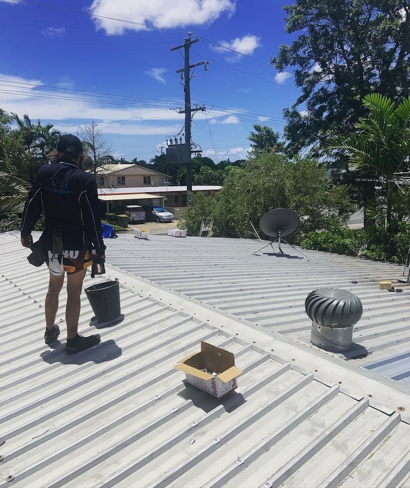 A Man is Standing on Top of a Roof With a Box on It — CJM Plumbing & Roofing Mackay in Sarina, QLD