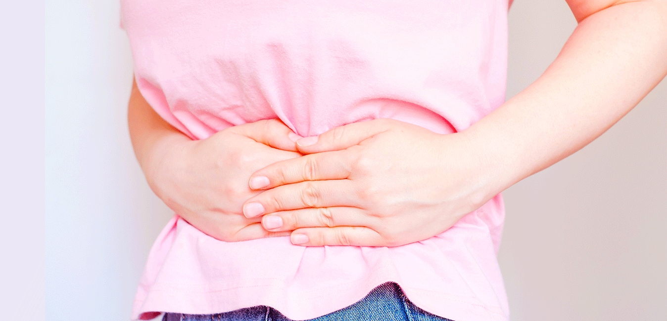 A woman in a pink shirt is holding her stomach in pain.