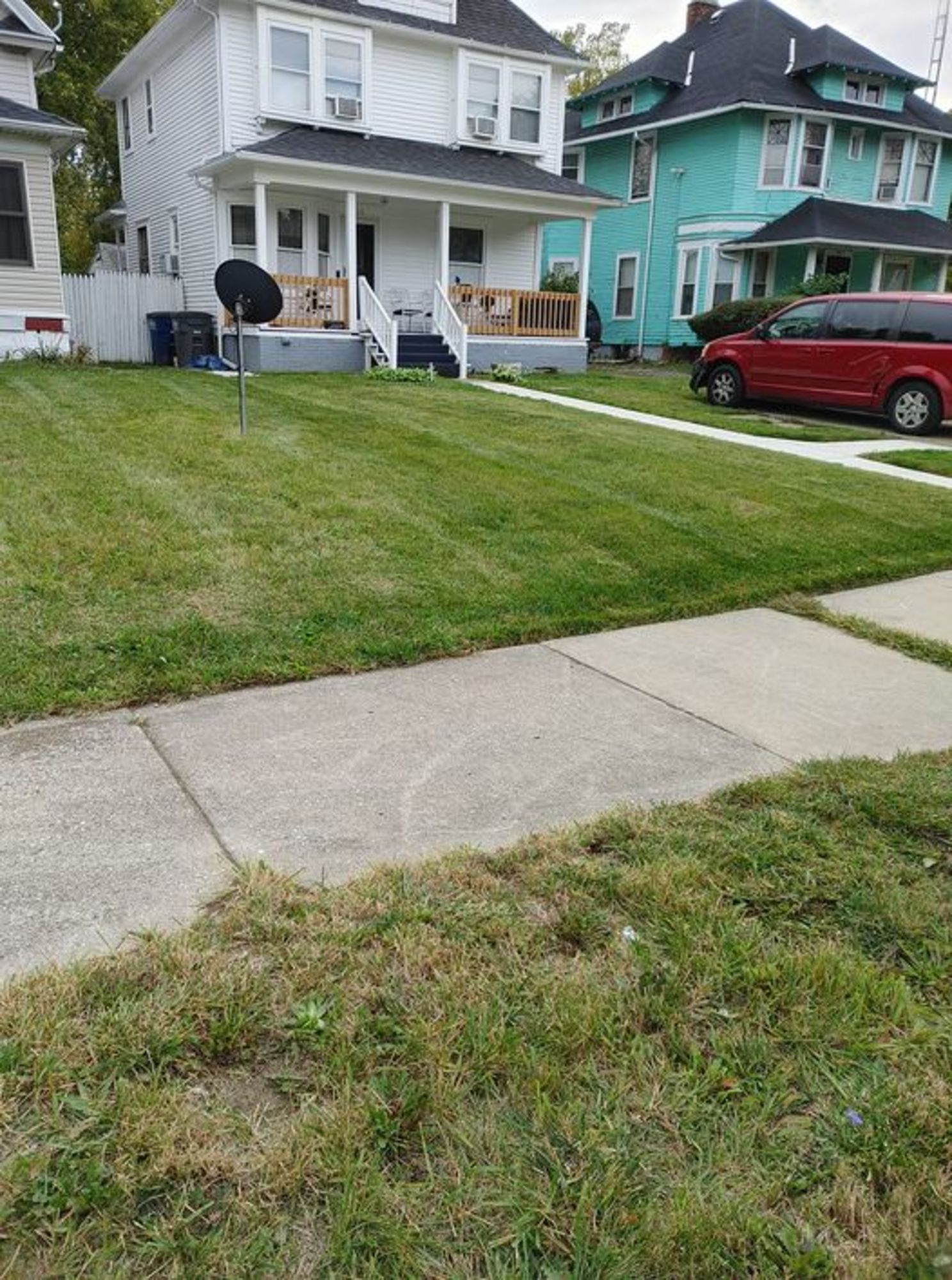 A red van is parked in front of a house with a lush green lawn.