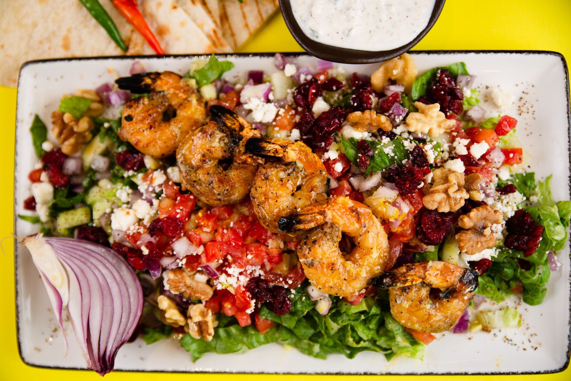 A salad with shrimp , lettuce , tomatoes , onions and walnuts on a plate.