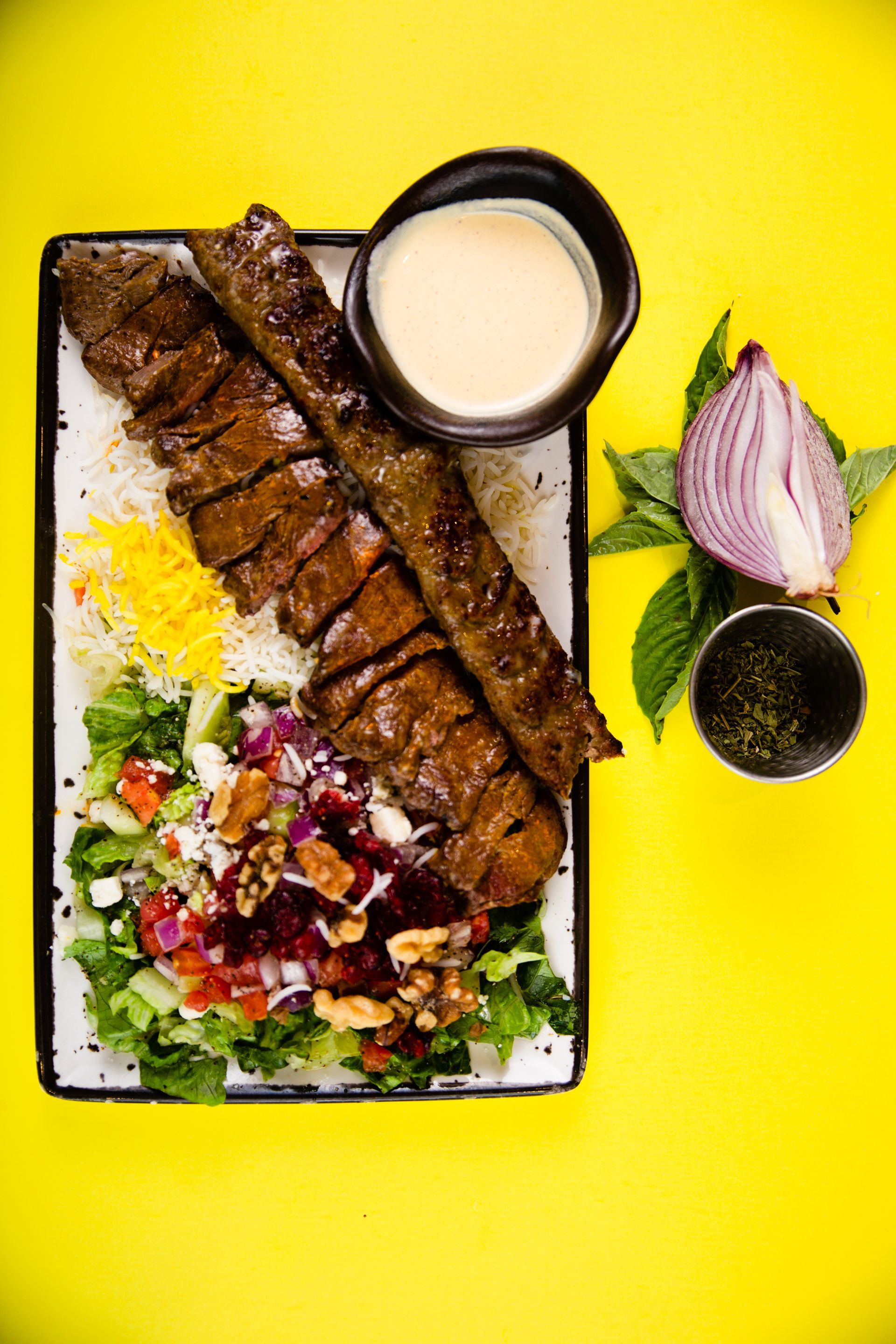 A plate of food with meat , rice , vegetables and sauce on a yellow background.