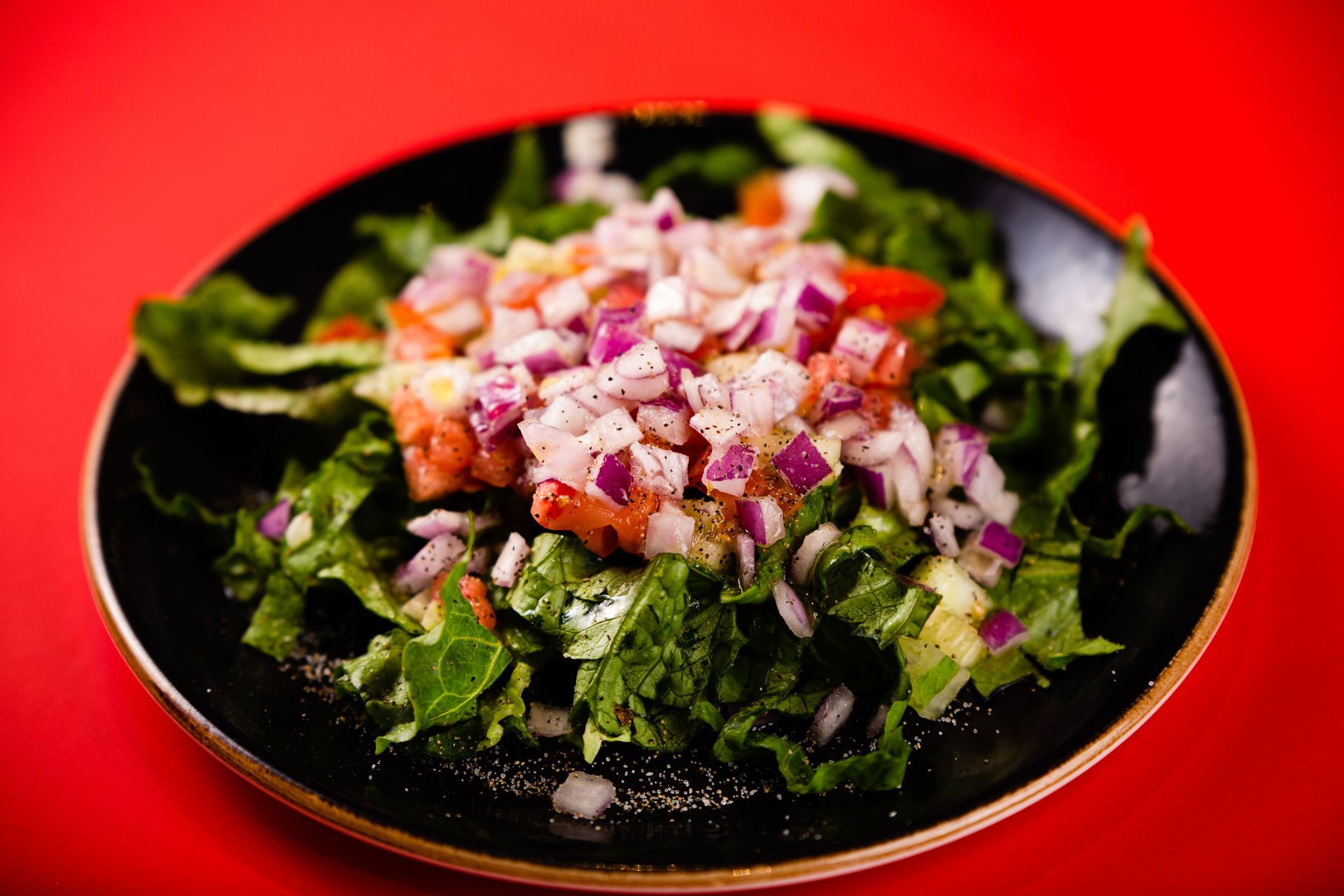 A close up of a salad on a black plate on a red table.