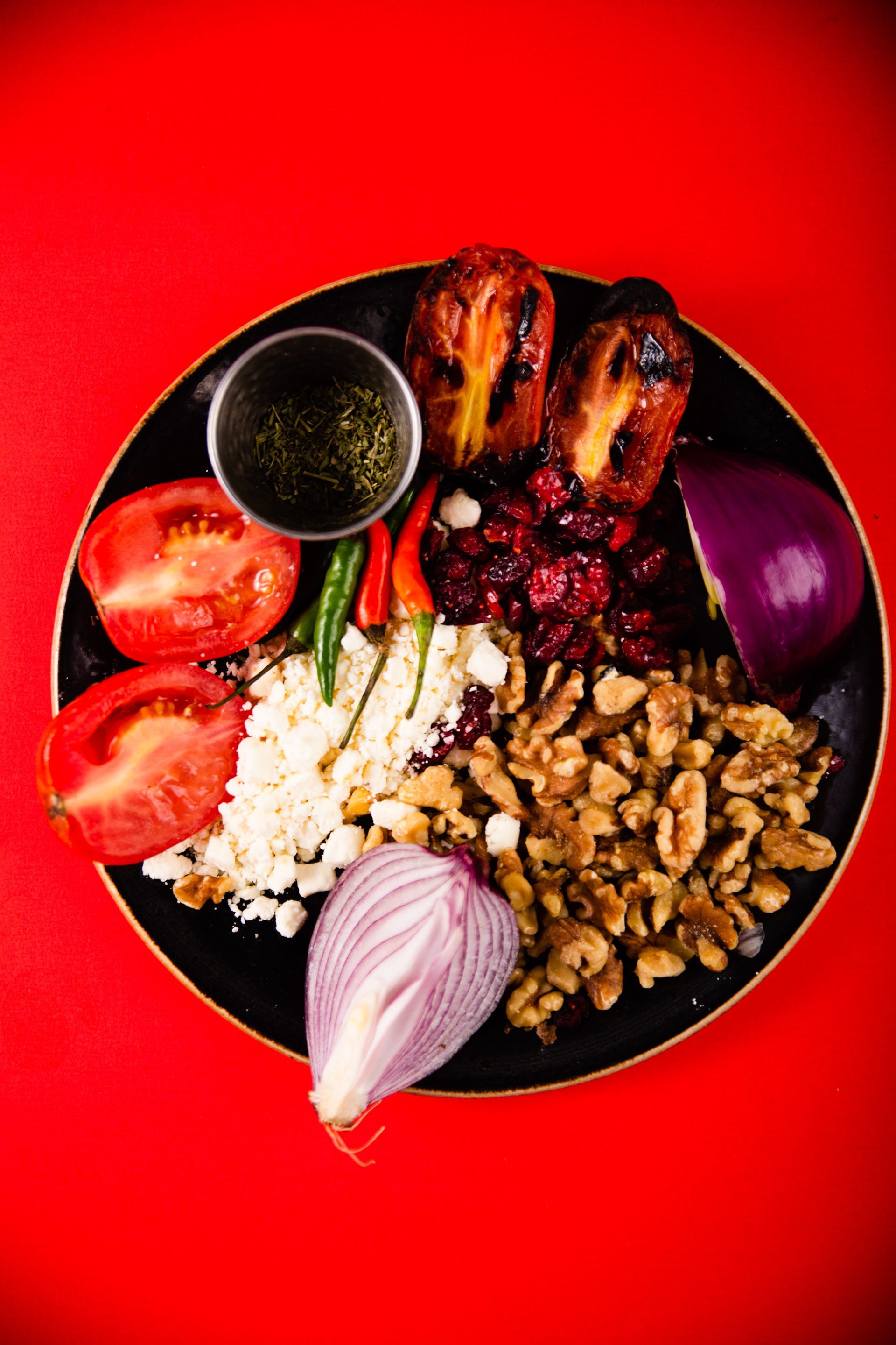 A black plate topped with vegetables and nuts on a red background.