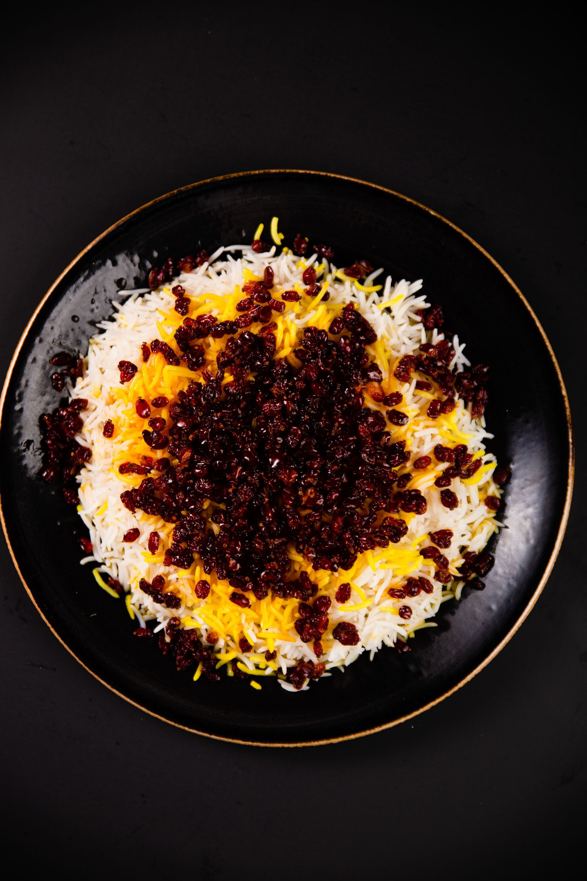 A black plate topped with rice and raisins on a black background.