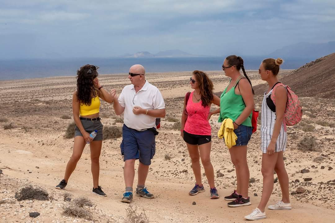 A group of people are standing in the desert talking and listening to Crazy David tour guide.
