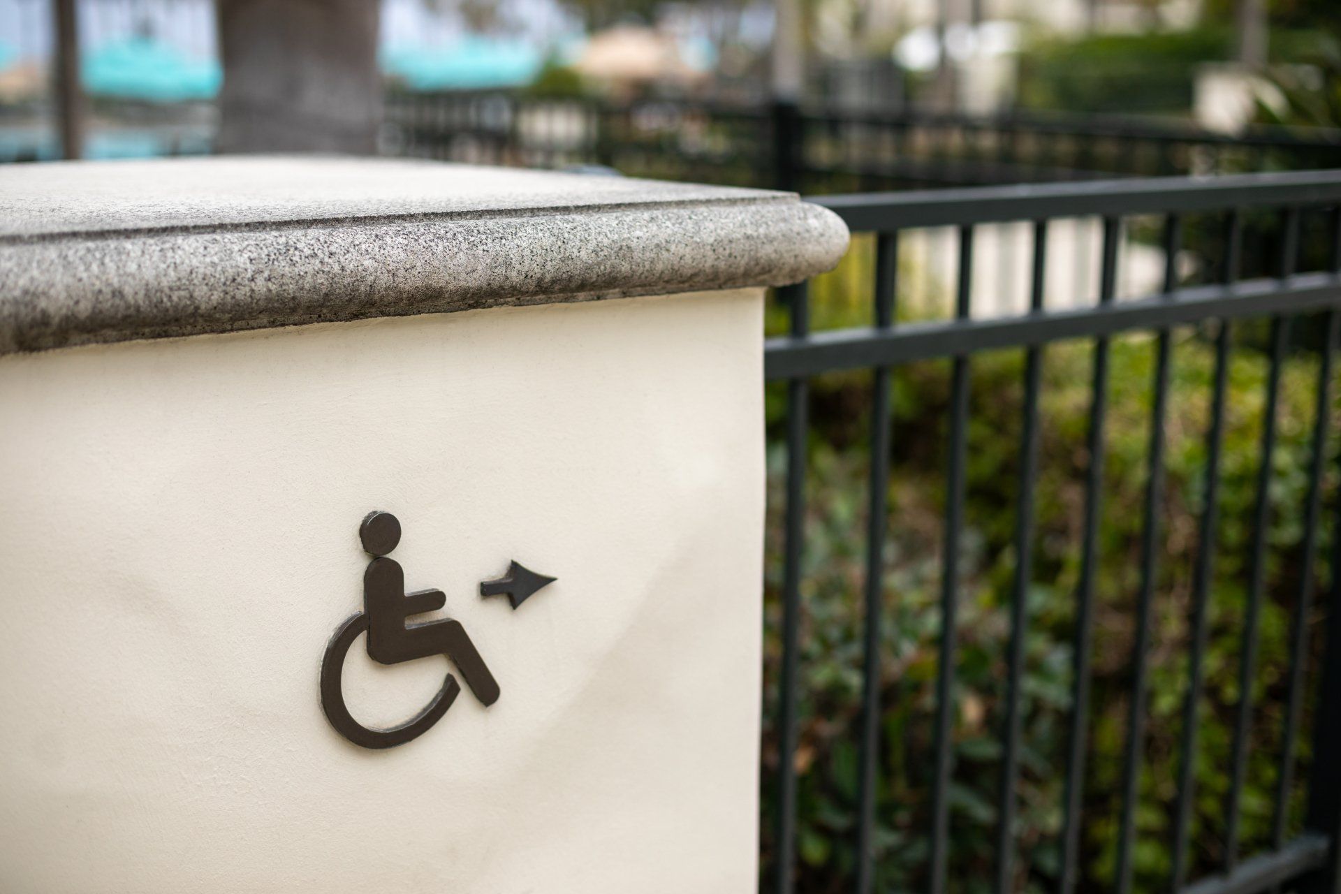 A handicap sign is painted on a white wall next to a fence.