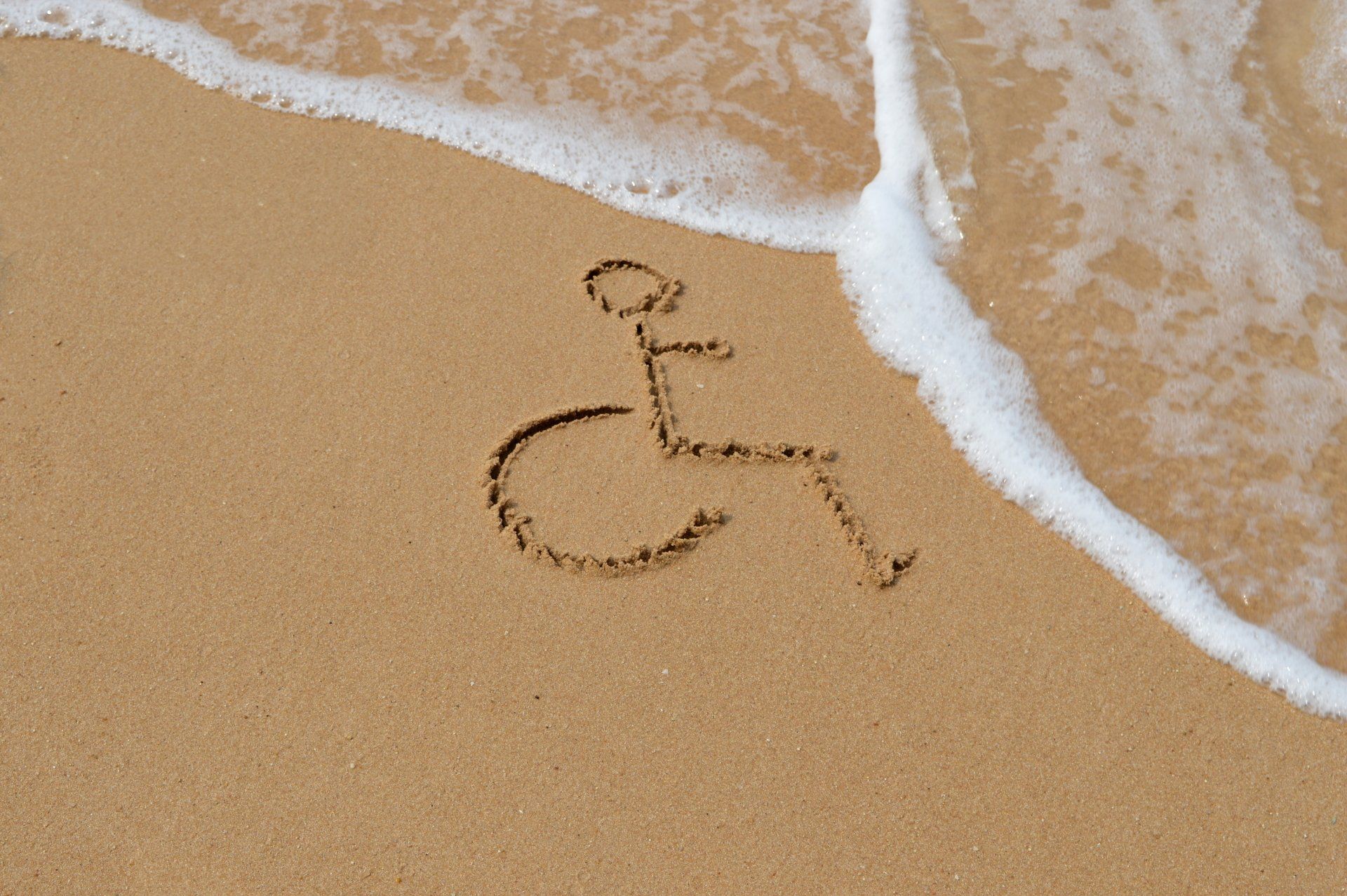 A wheelchair is drawn in the sand on the beach.