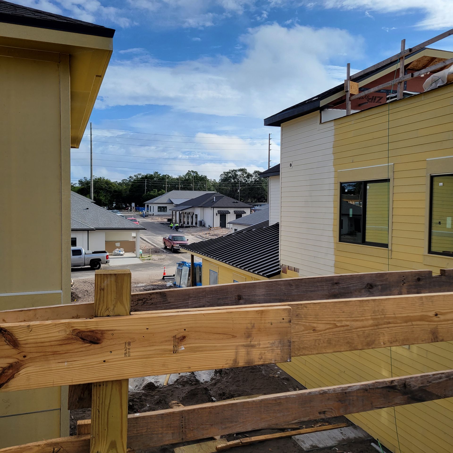 Construction site with partially built houses under a blue sky. Wooden beams in the foreground.