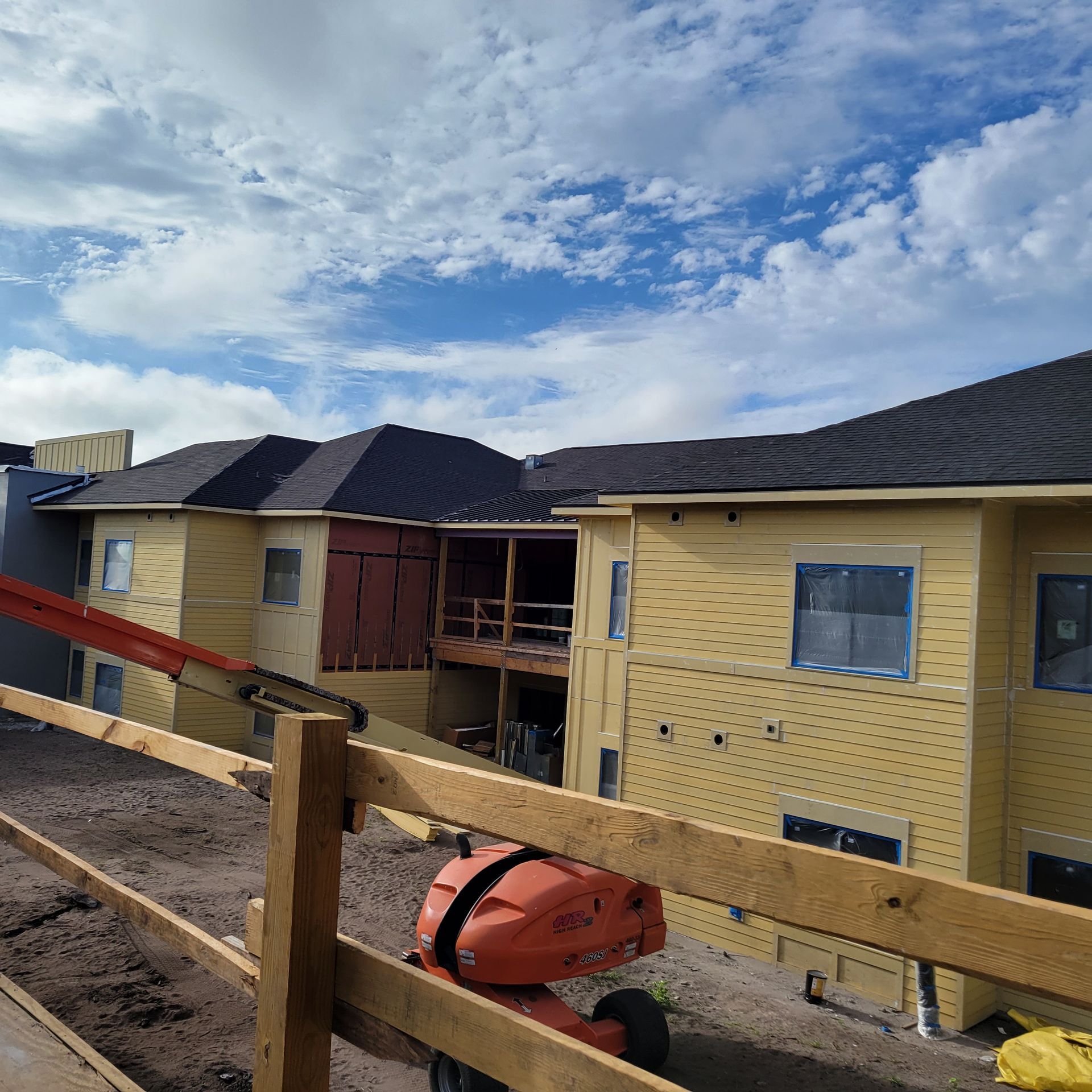 Building under construction with yellow siding, black roof, wooden frame, blue sky.