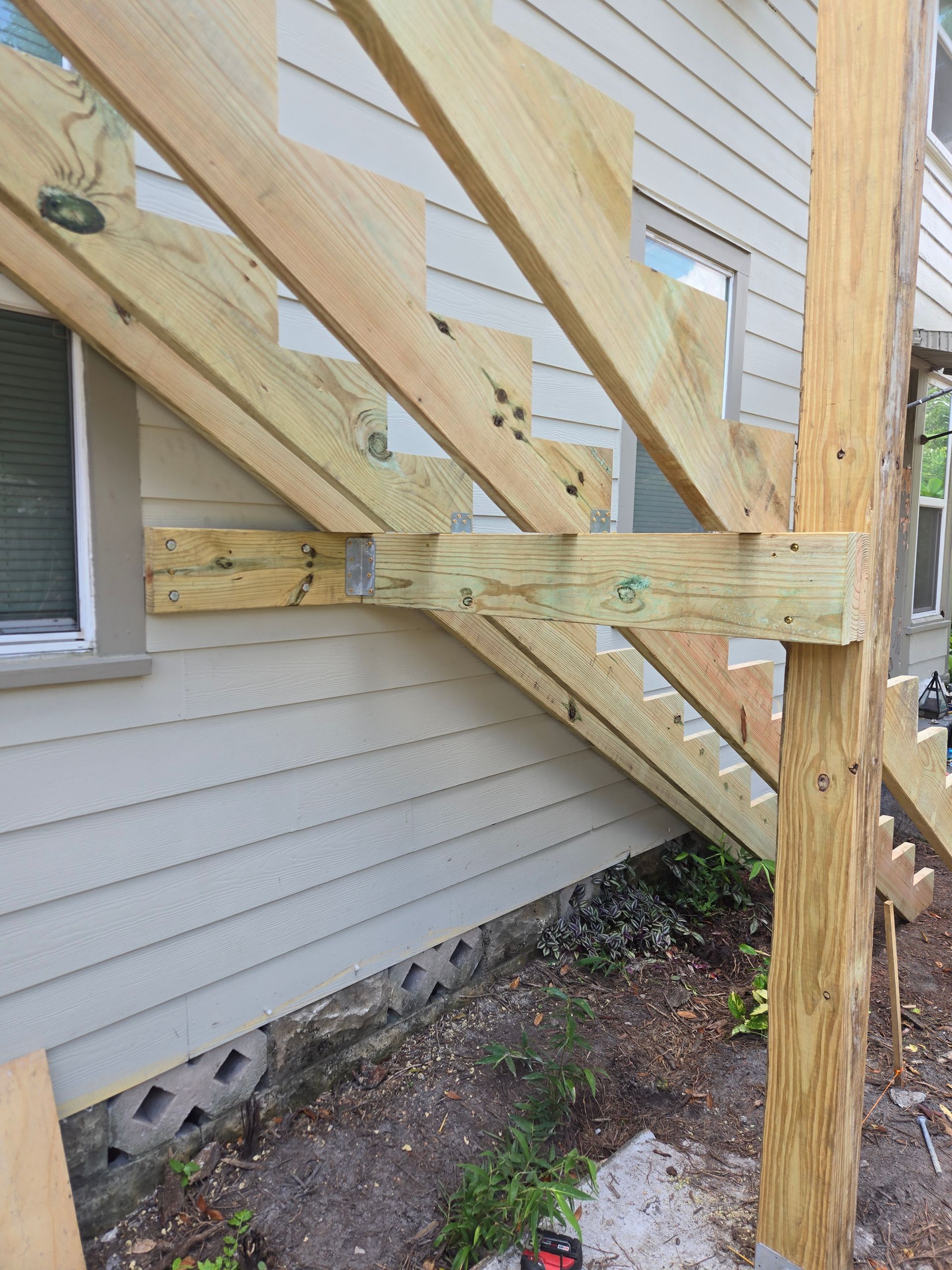 Wooden staircase construction next to a house with pressure-treated lumber and metal brackets.