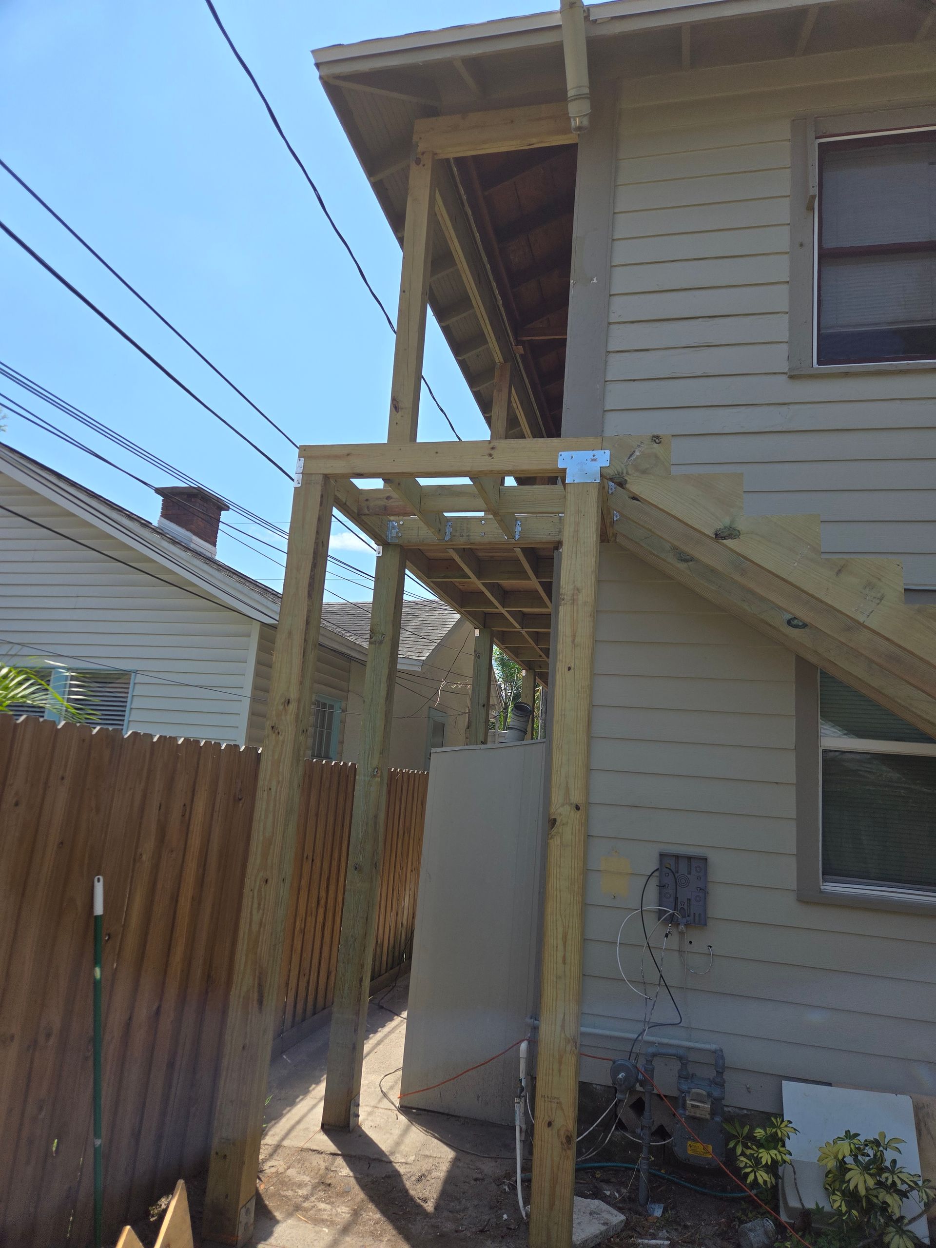 Wooden deck construction with stairs against a house, utility pole lines in the background.
