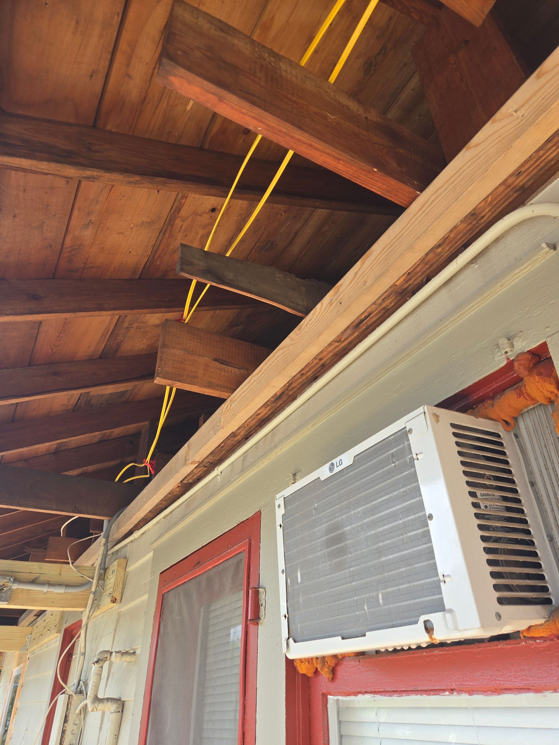 Wooden porch ceiling with exposed beams, yellow wiring, and an air conditioning unit.