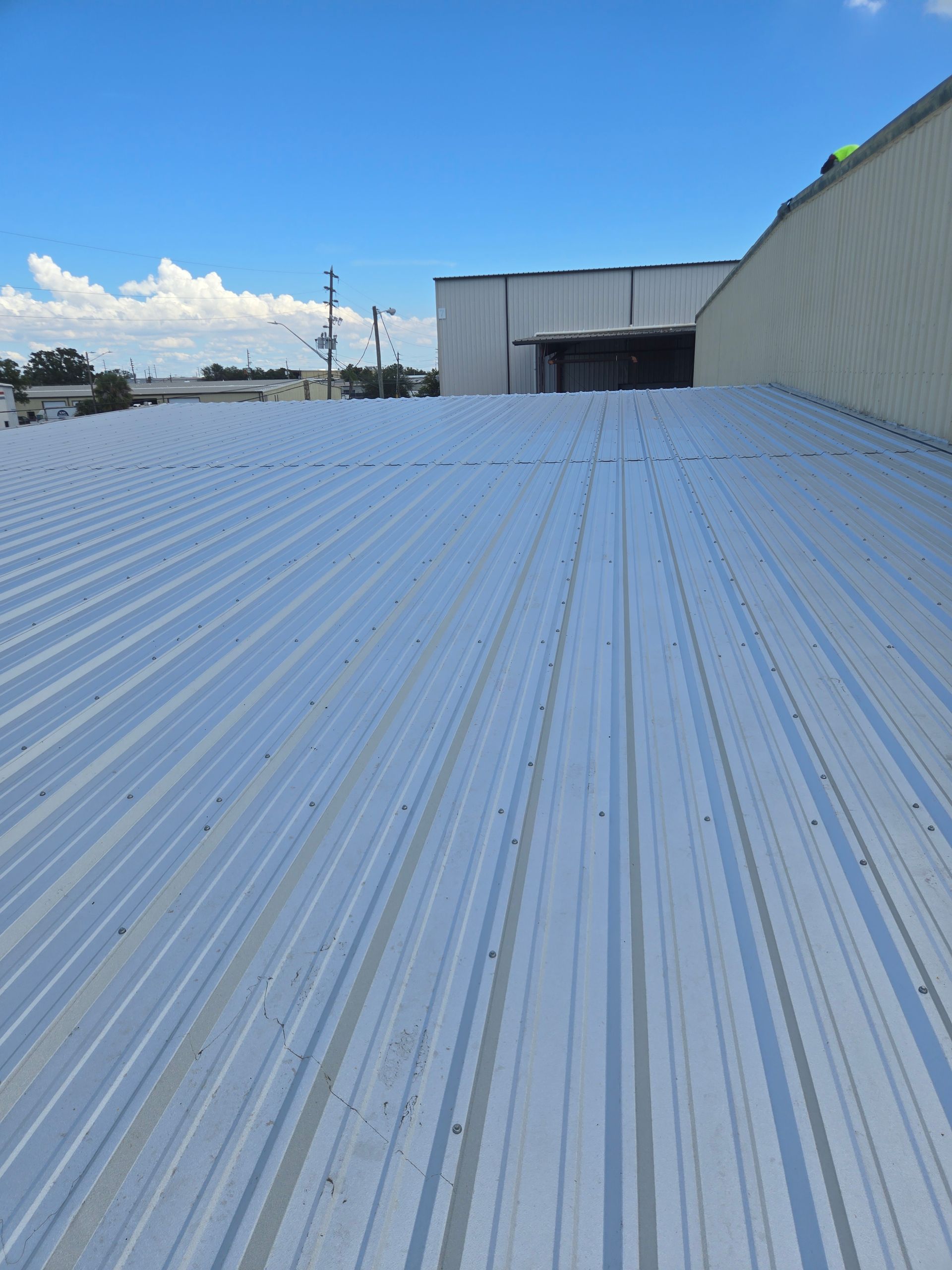 Metal roof on a building under a bright blue sky with scattered clouds.