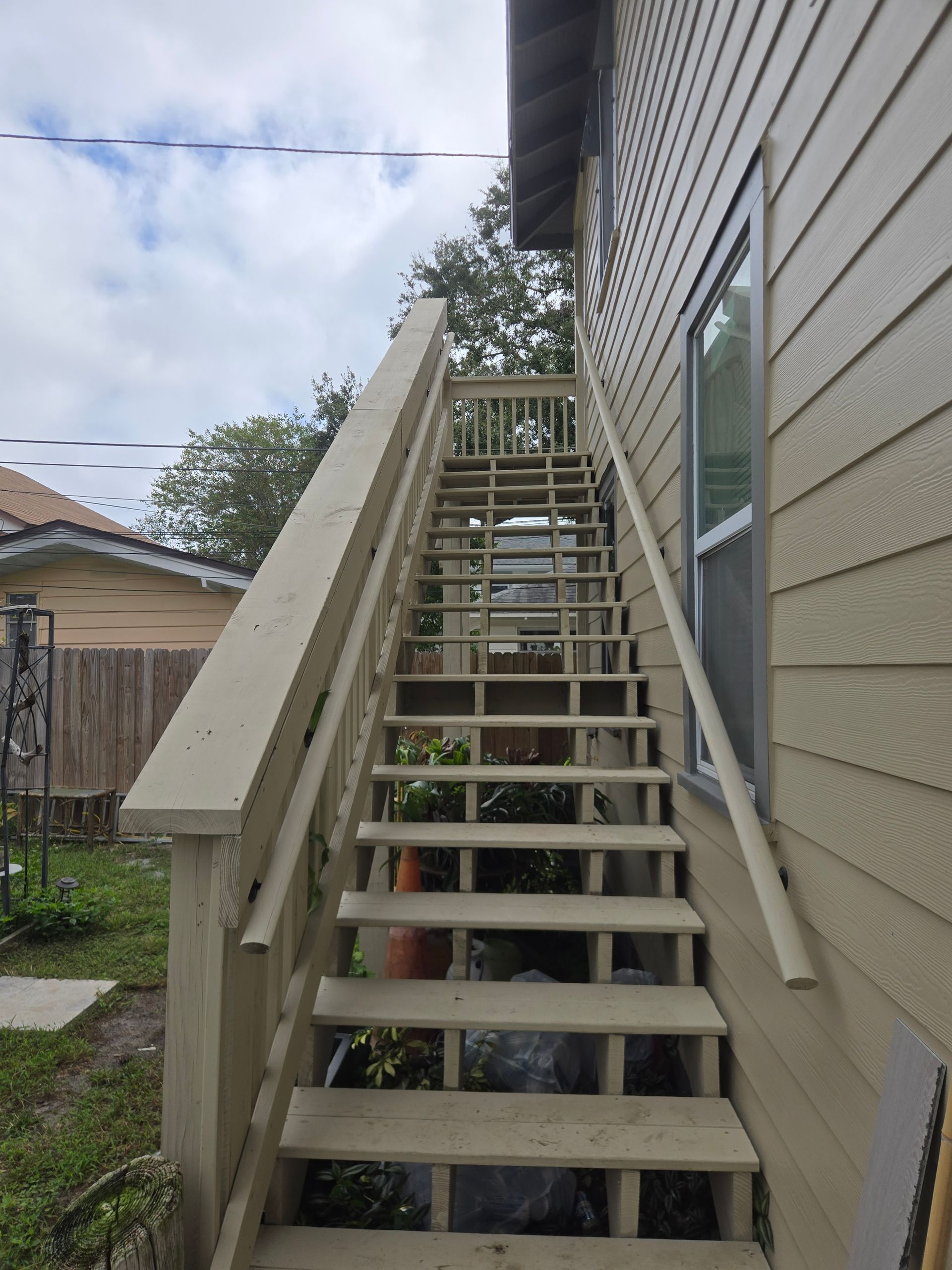 Outdoor wooden staircase leading up a building with beige siding. Cloudy sky background.