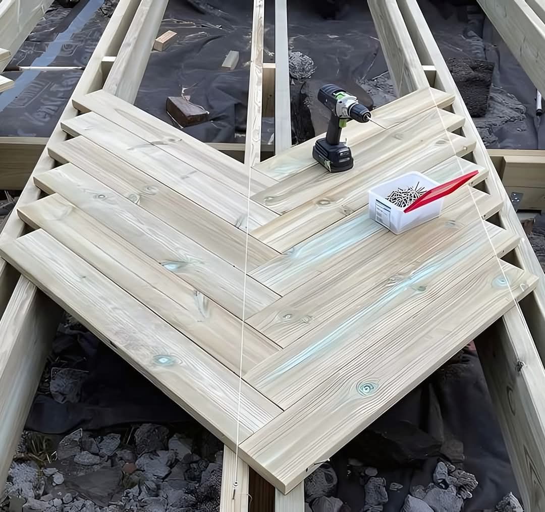 Herringbone wood deck construction in progress; a drill, screws, and boards sit atop the frame.