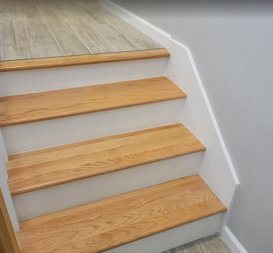 Wooden staircase with white risers and gray walls.