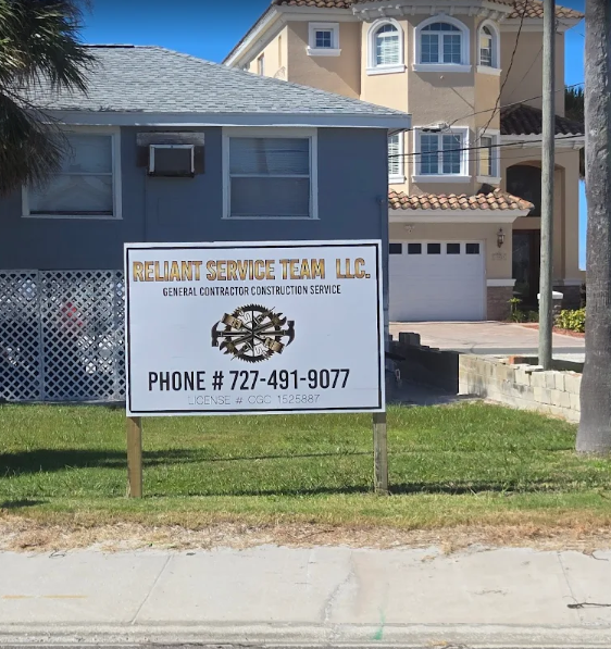 Sign for Belmont Service Team LLC, with phone number, in front of blue building and beige house.