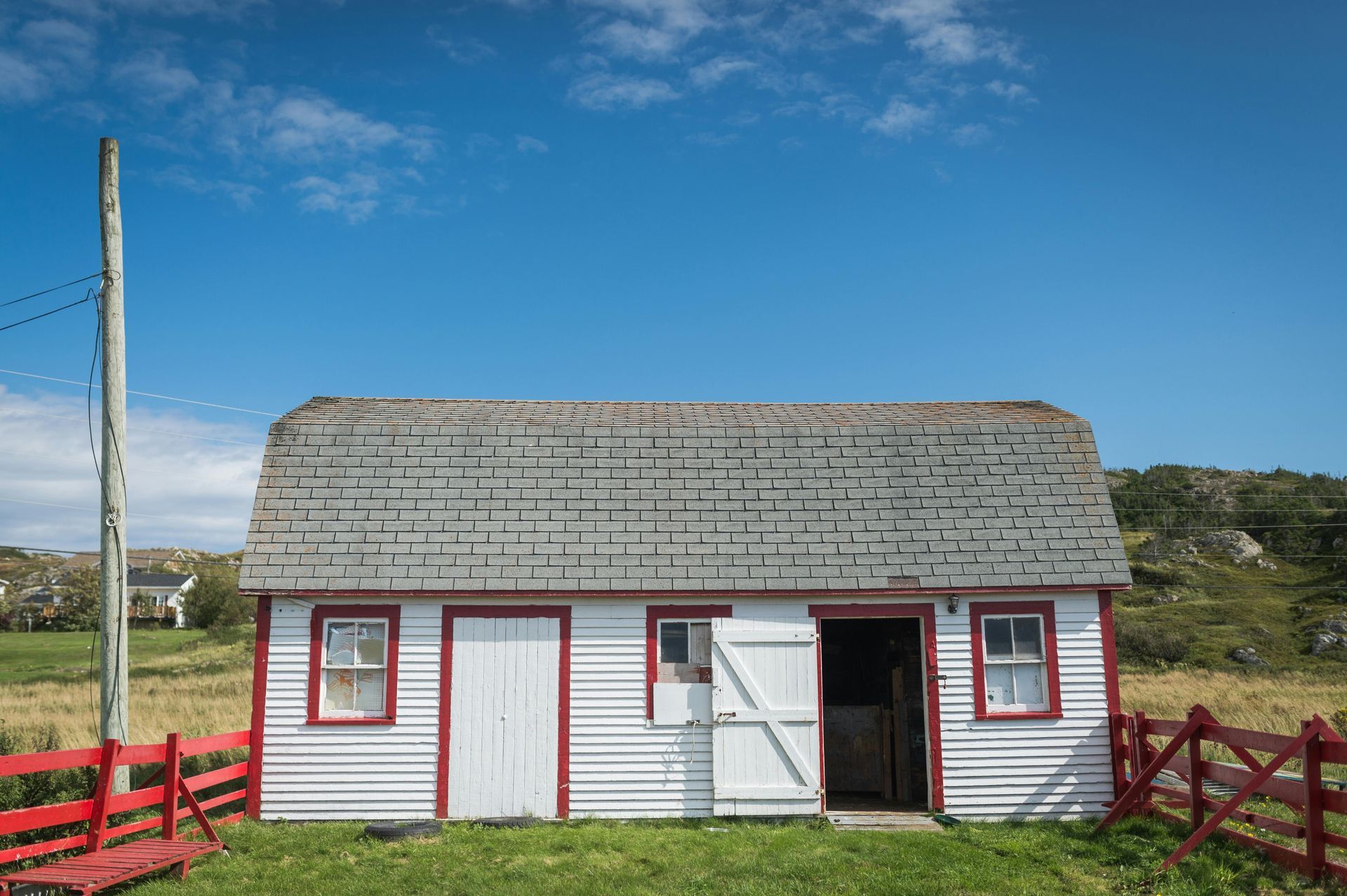 White shed with red trim and fence against a bright blue sky.