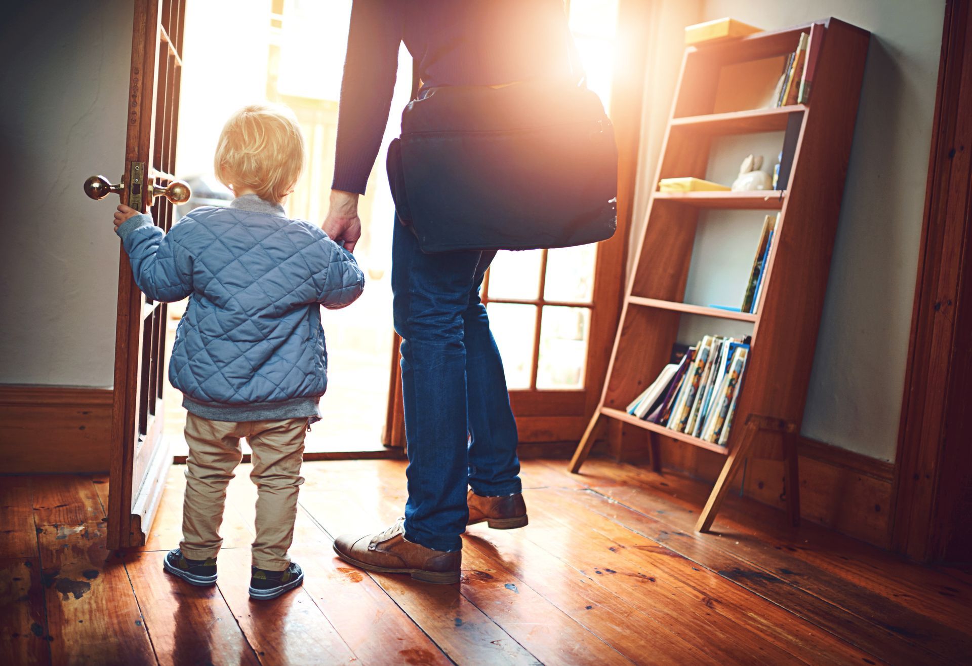 A man and a child are standing in a hallway holding hands.