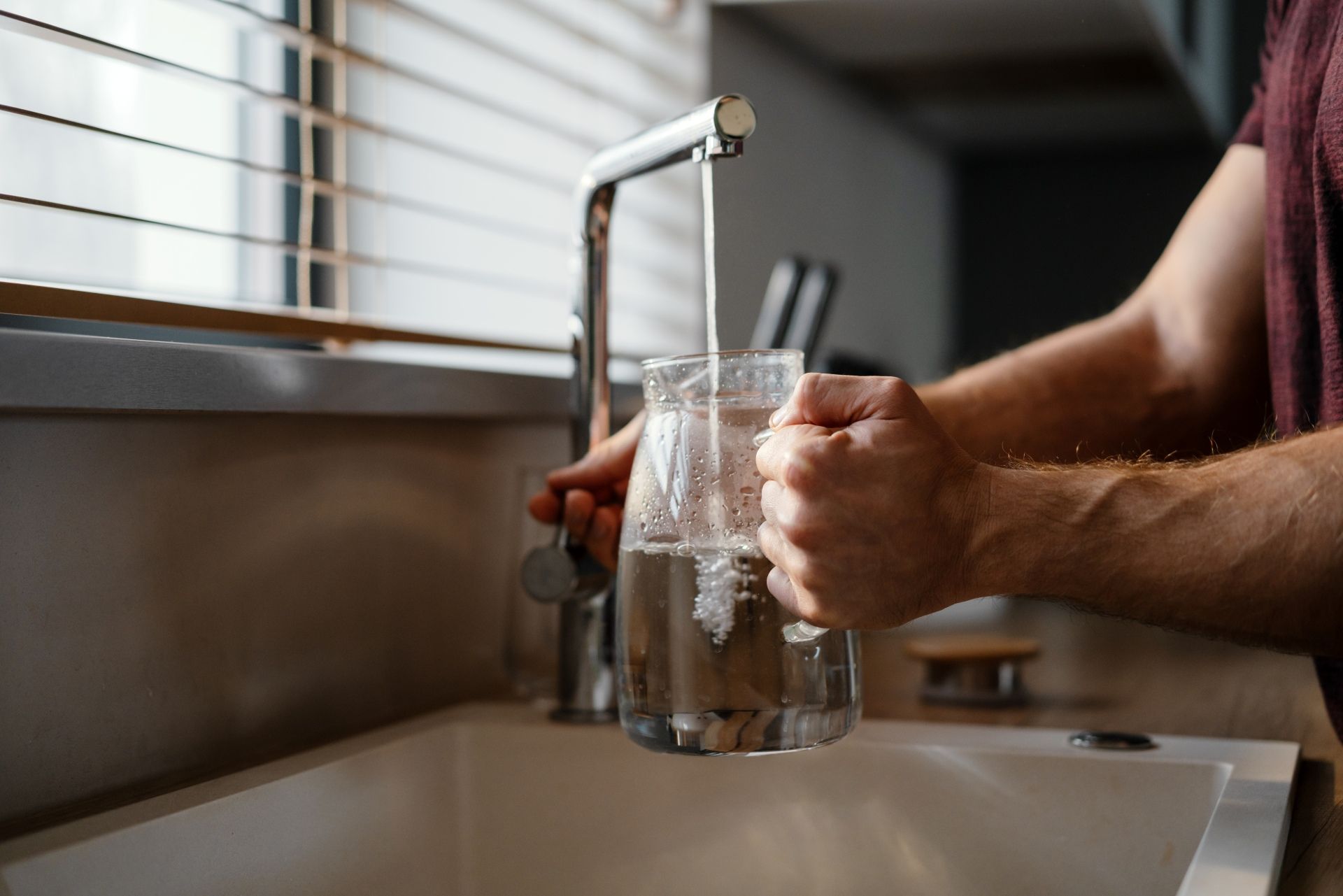 Person filling a glass pitcher with water from a kitchen faucet.