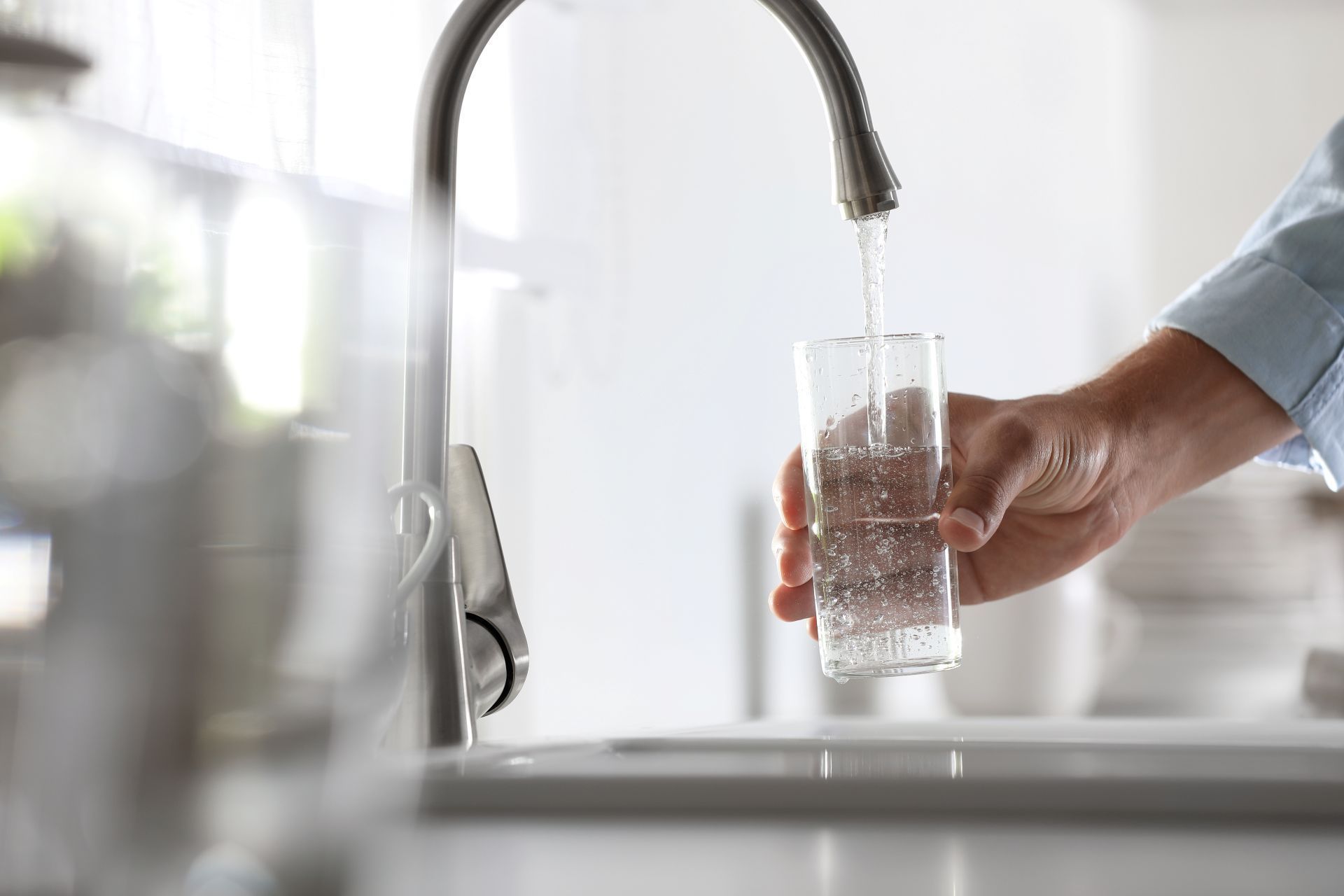 Person filling a glass with water from a kitchen faucet.
