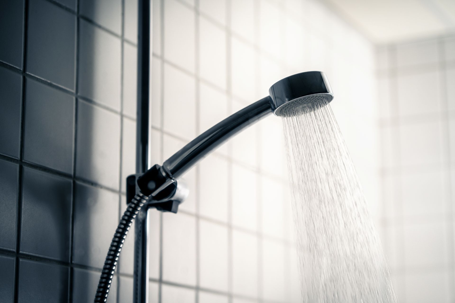 Shower head with water spraying against tiled wall.